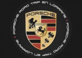 L'image représente le logo Porsche avec un cheval noir, des bandes rouges et noires et des bois. Autour, "Porsche Road Trip en Lorraine" est inscrit dans un cercle sur fond noir, célébrant ainsi les clubs indépendants et leur passion pour la conduite.
