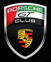 Un emblème en forme de bouclier avec "Porsche GT Club" en haut en rouge, vert, noir et blanc, et l'écusson jaune de Porsche avec un cheval noir et des bois en dessous sur un fond noir en fibre de carbone.